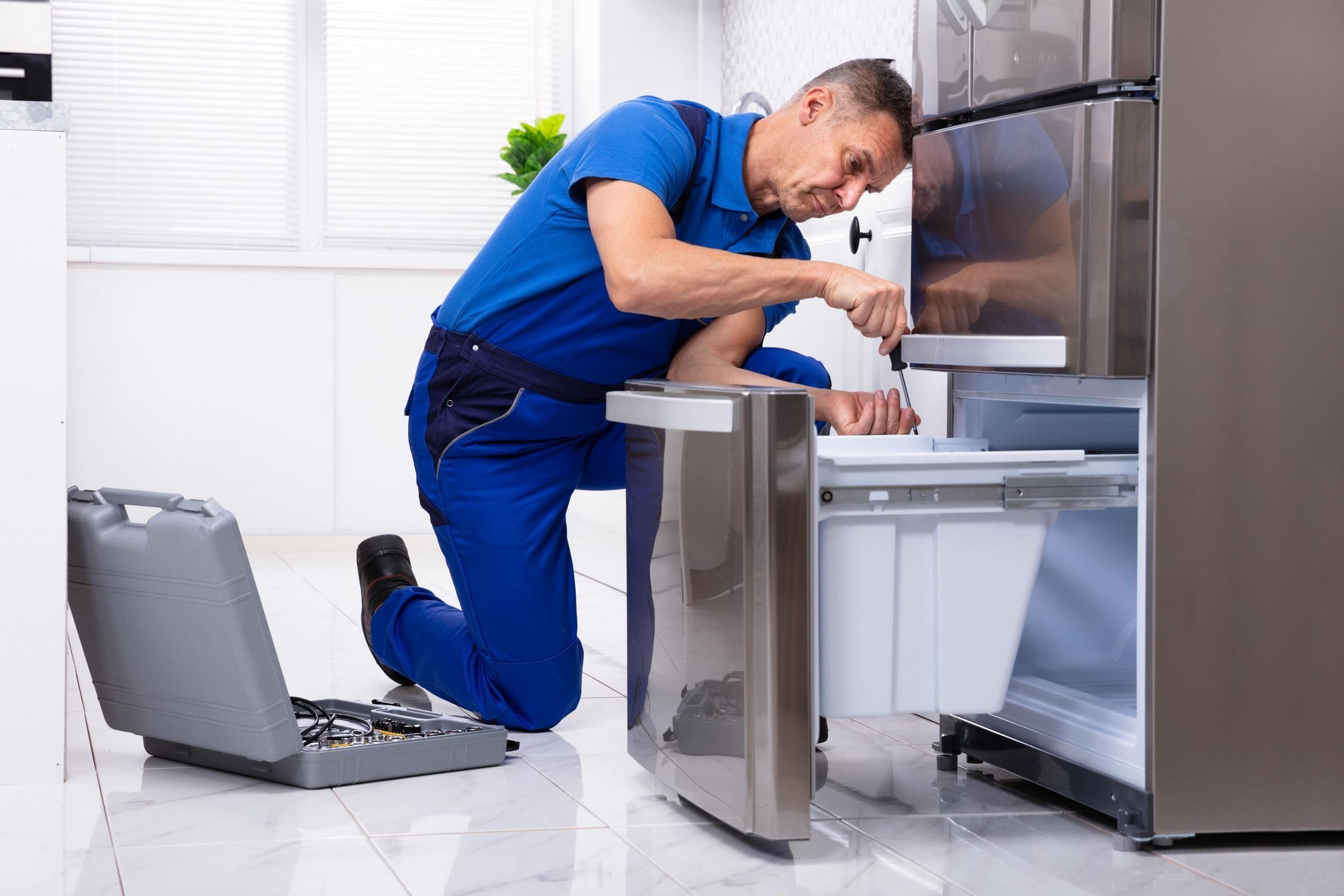 Professional fixing a double-door fridge in a Dubai apartment.